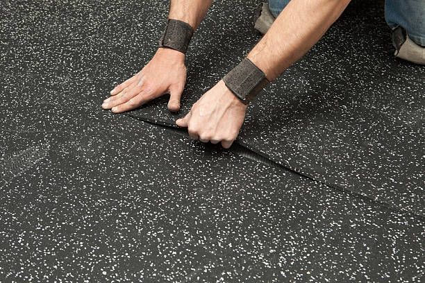 A person is laying a piece of rubber flooring on the ground.