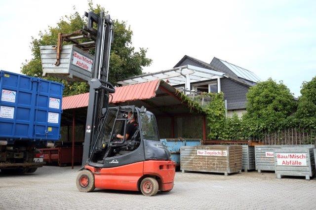 Roter Gabelstapler von Dachdeckerei Hübler und Glatz GmbH hebt Müll in blauen LKW