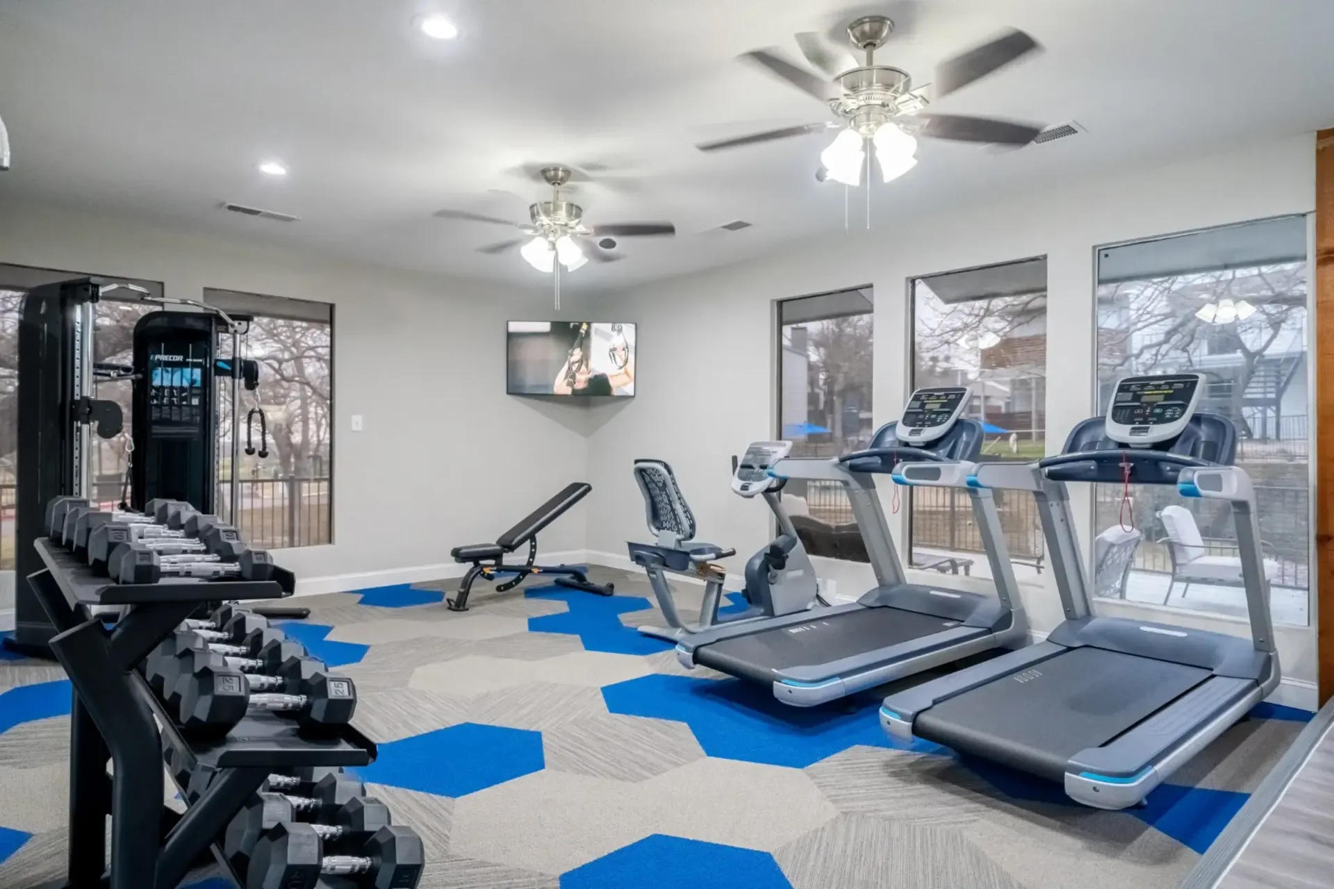 A gym with treadmills , dumbbells , and a ceiling fan.