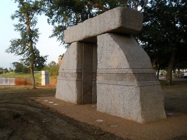 Large stone archway sculpture in a park setting.