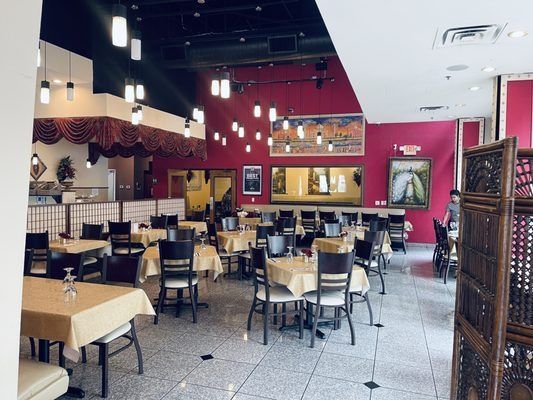Restaurant interior with tables, chairs, and maroon walls, decorated with lights and art.