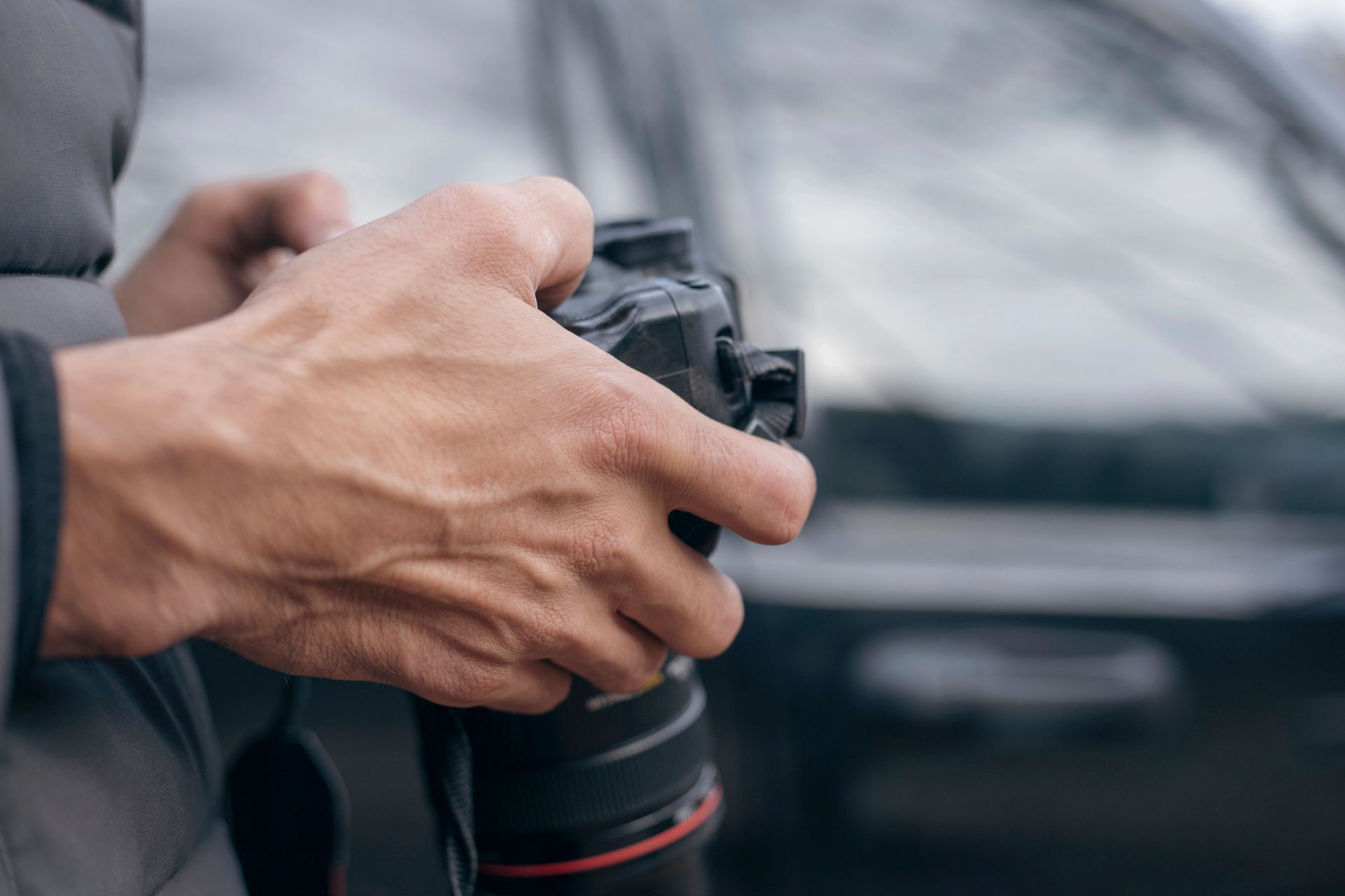 Primo piano di mani che reggono una fotocamera reflex digitale professionale davanti a un veicolo sfocato.
