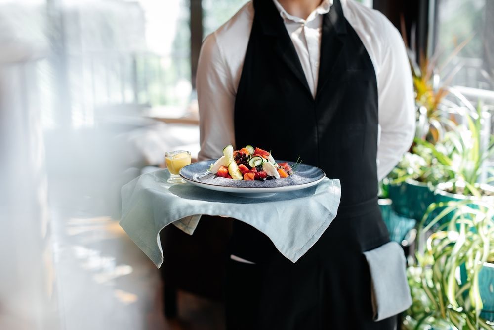 Waiter holding tray with a salad and juice, in a restaurant.