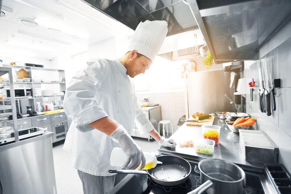 Chef in white uniform cooking in a stainless steel commercial kitchen.