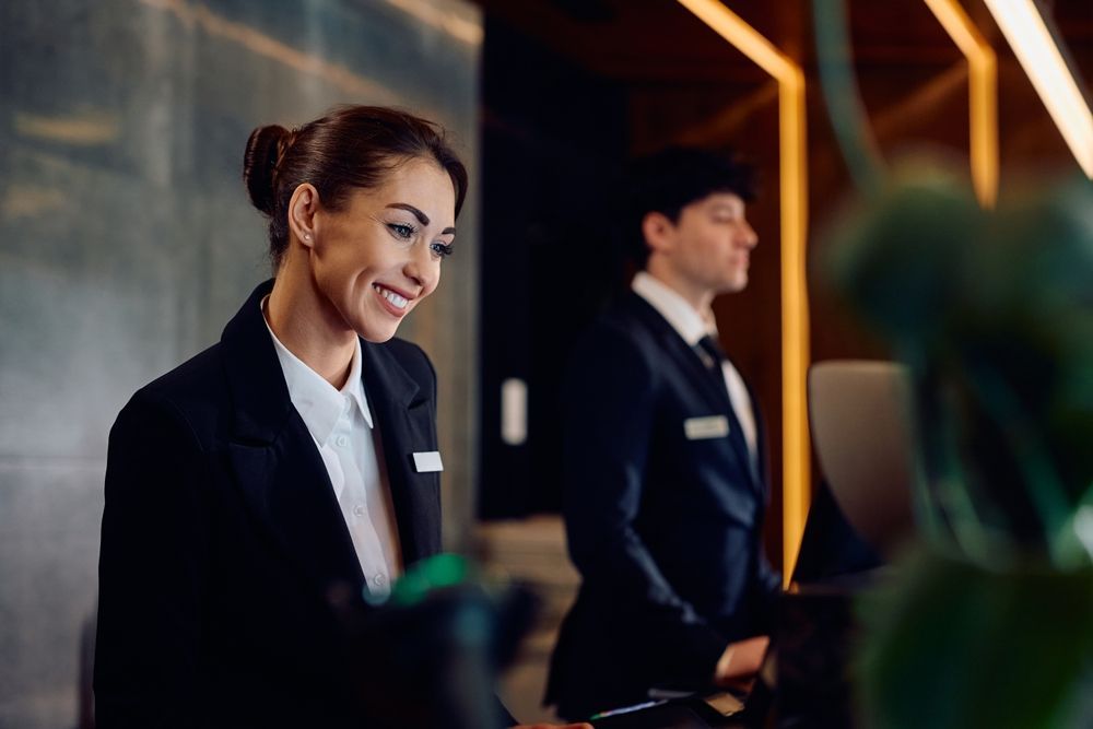 Smiling hotel receptionist at a front desk, with a colleague behind her.