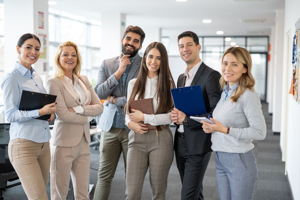 Business team of six in a modern office, smiling and posing with notepads.