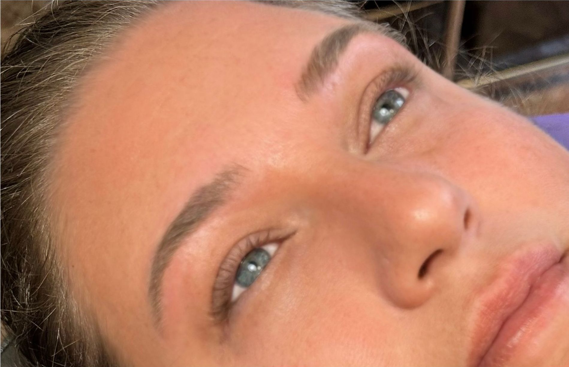 A woman is getting her eyebrows painted by a makeup artist.