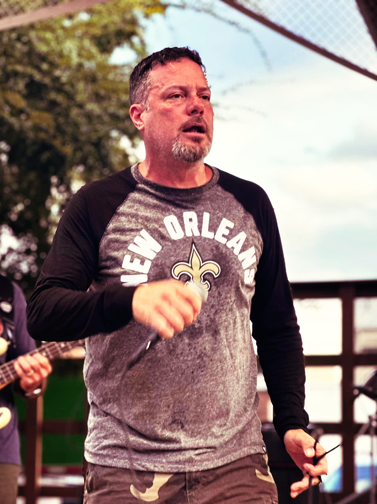 Man singing into a microphone on stage, wearing a New Orleans Saints shirt.