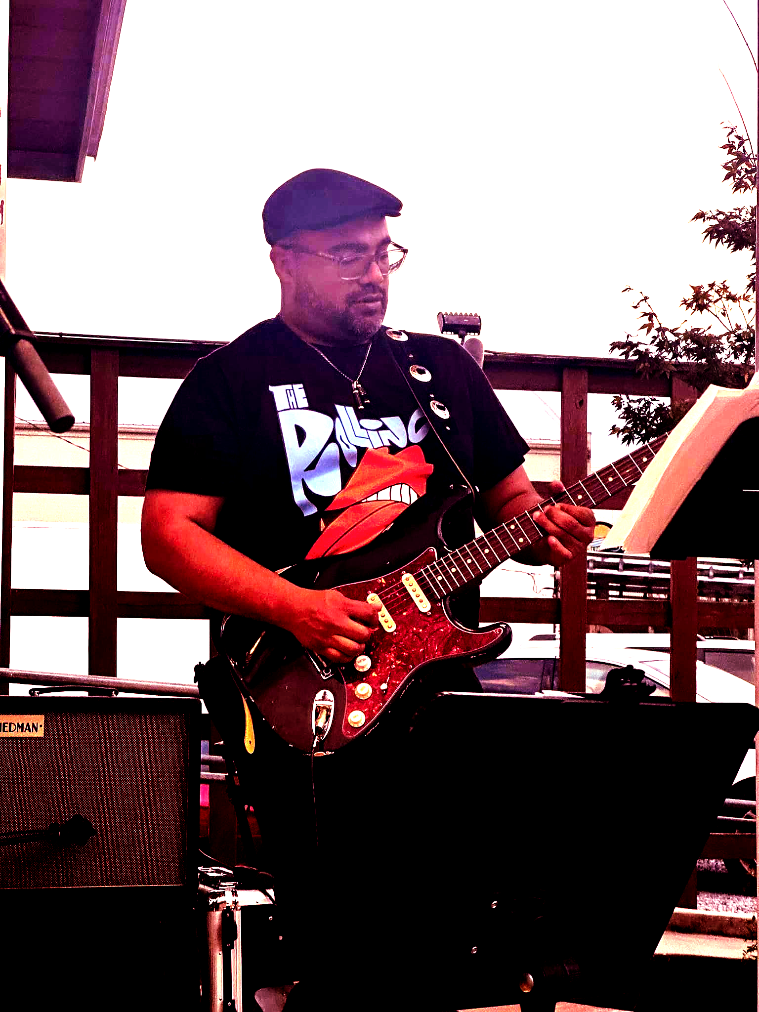 Man playing electric guitar on a stage, wearing a black shirt and hat.
