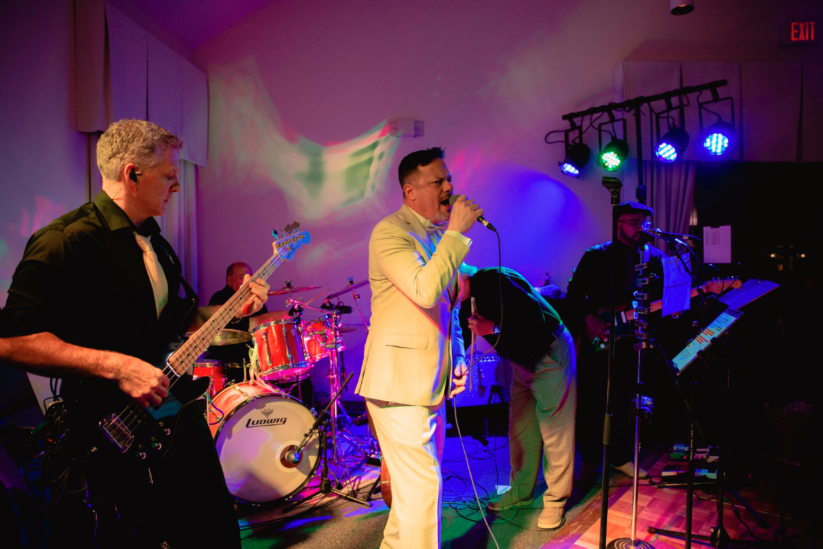 Band performing on stage under colorful lights; vocalist sings into a microphone.