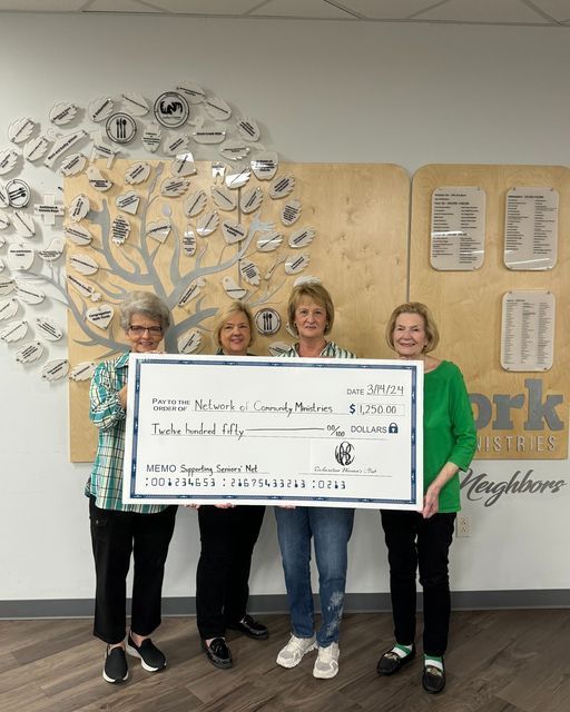 A group of women holding a large check in front of a wall that says neighbors