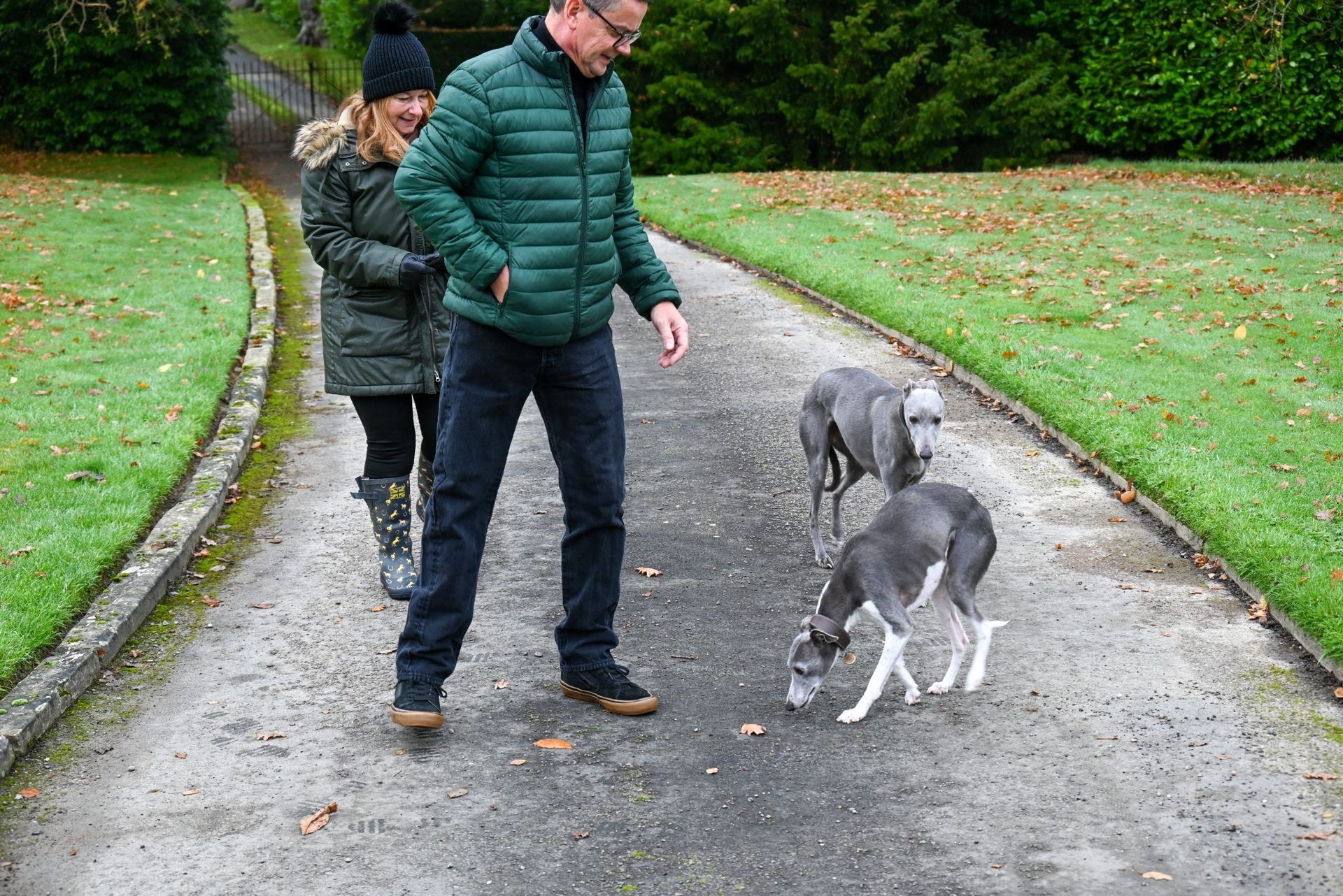 A man and a woman are walking a dog down a path.