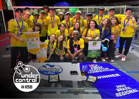 A group of people wearing yellow shirts celebrate with trophies and banners at the FIRST Robotics Competition in Brazil.