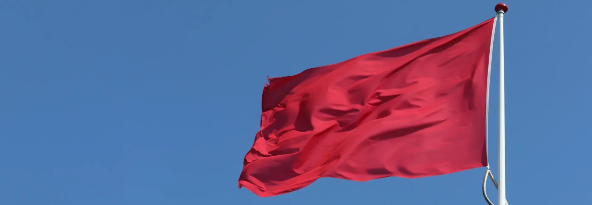 A red flag is waving in the wind against a blue sky.