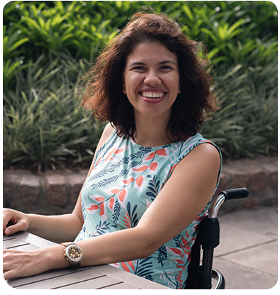 A woman in a wheelchair is smiling while sitting at a table.