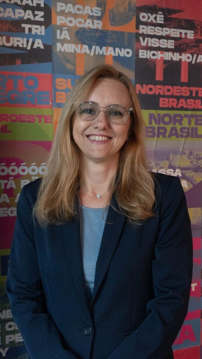 A woman in a suit and glasses is smiling in front of a colorful wall.