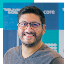 A man wearing glasses is smiling in front of a wall that says core