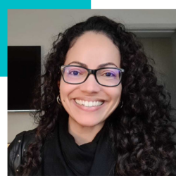 A woman with curly hair wearing glasses and a black scarf is smiling.