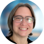 Woman with glasses, smiling, with short gray hair, set against a blurred blue background.