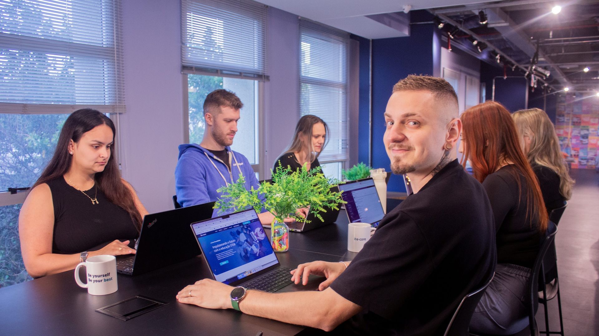 6 people with laptops, working in a table, blue background