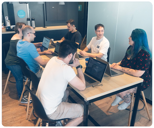 Um grupo de pessoas está sentado ao redor de uma mesa com laptops.