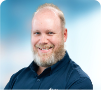 A man with a beard is wearing a blue shirt and smiling.