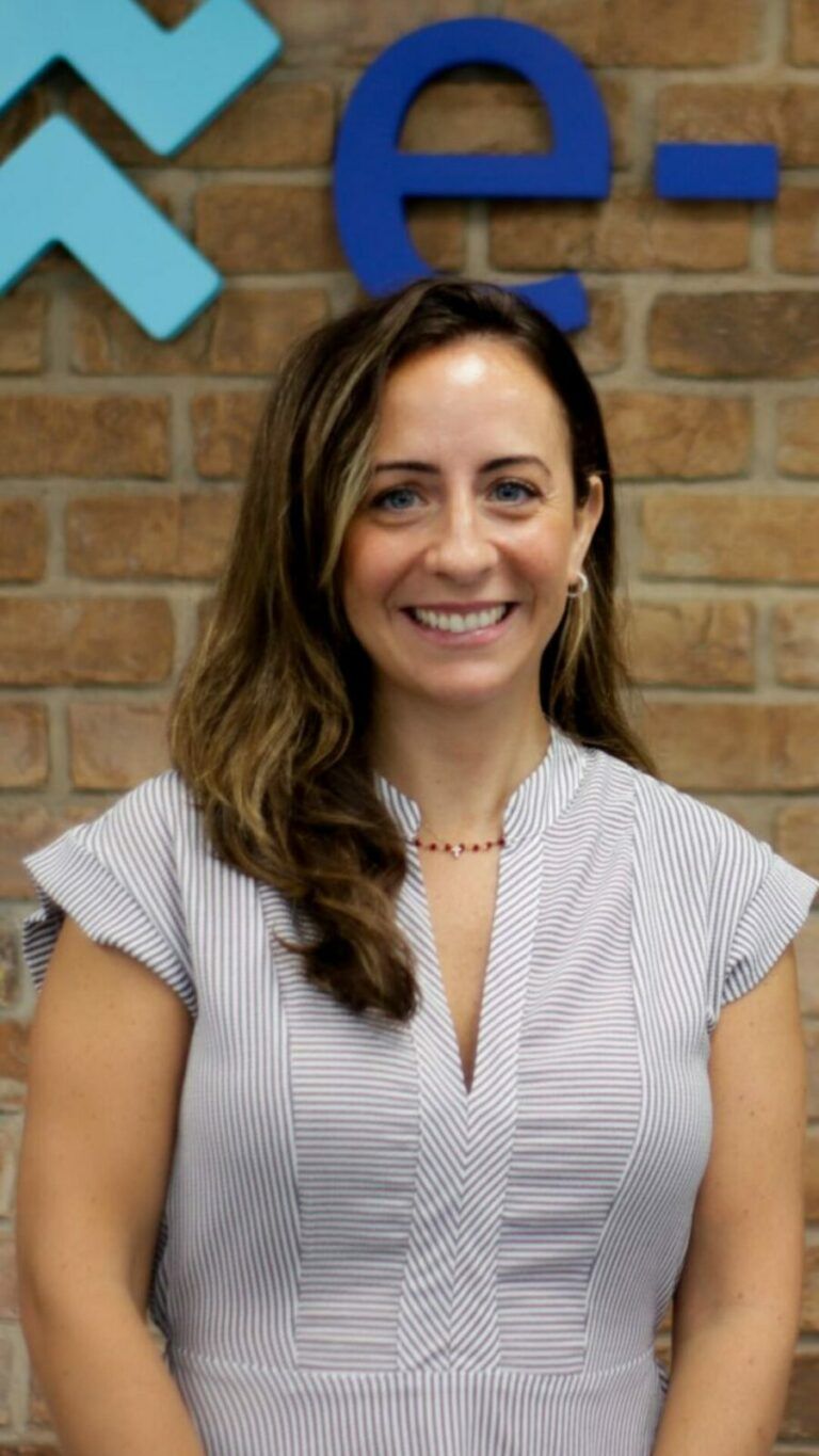 A woman in a suit and glasses is smiling in front of a colorful wall.