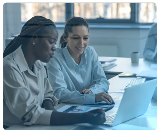 Duas mulheres estão sentadas à mesa olhando para um laptop.