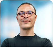 A man wearing glasses and a black shirt is smiling with his arms crossed.
