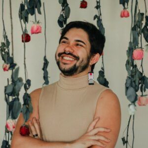 A man with a beard is smiling in front of a wall of flowers.