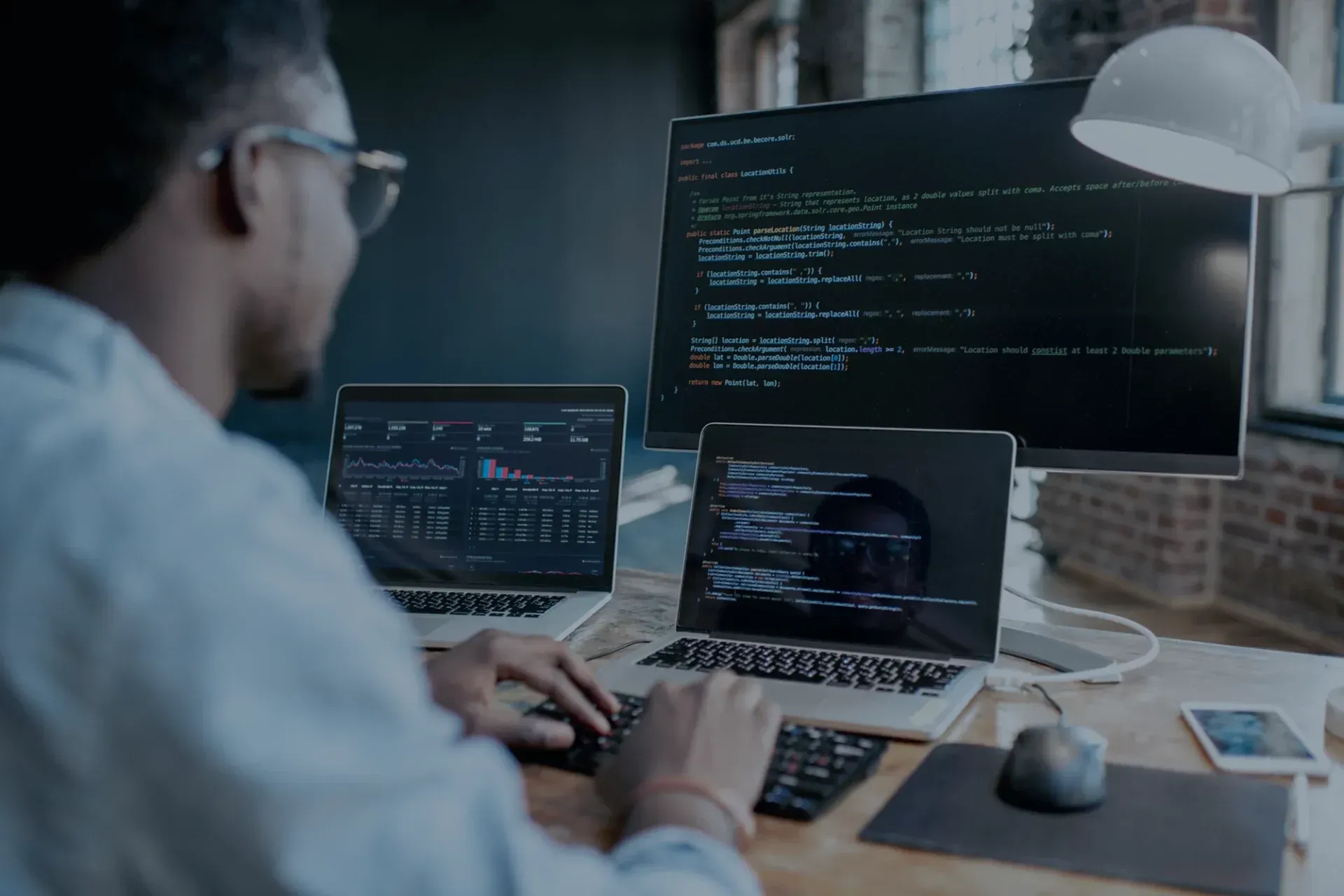 Um homem está sentado em uma mesa usando um laptop e um computador.