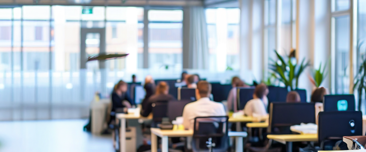 People working at computers in a bright, modern office with large windows.