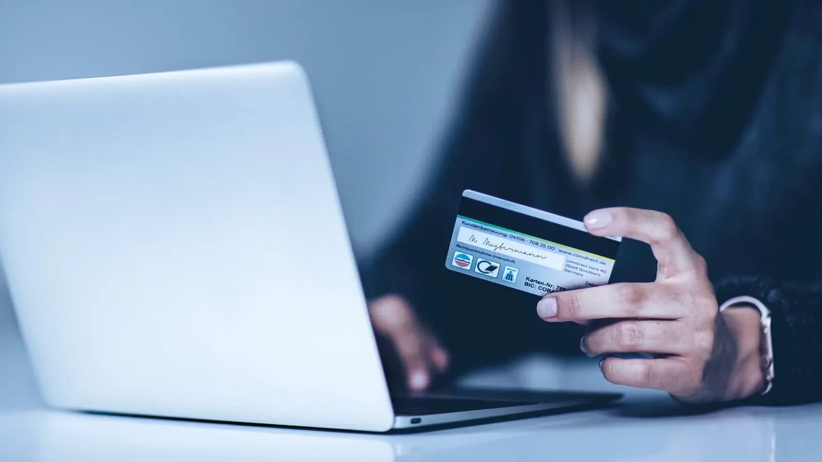 A person is holding a credit card in front of a laptop computer.