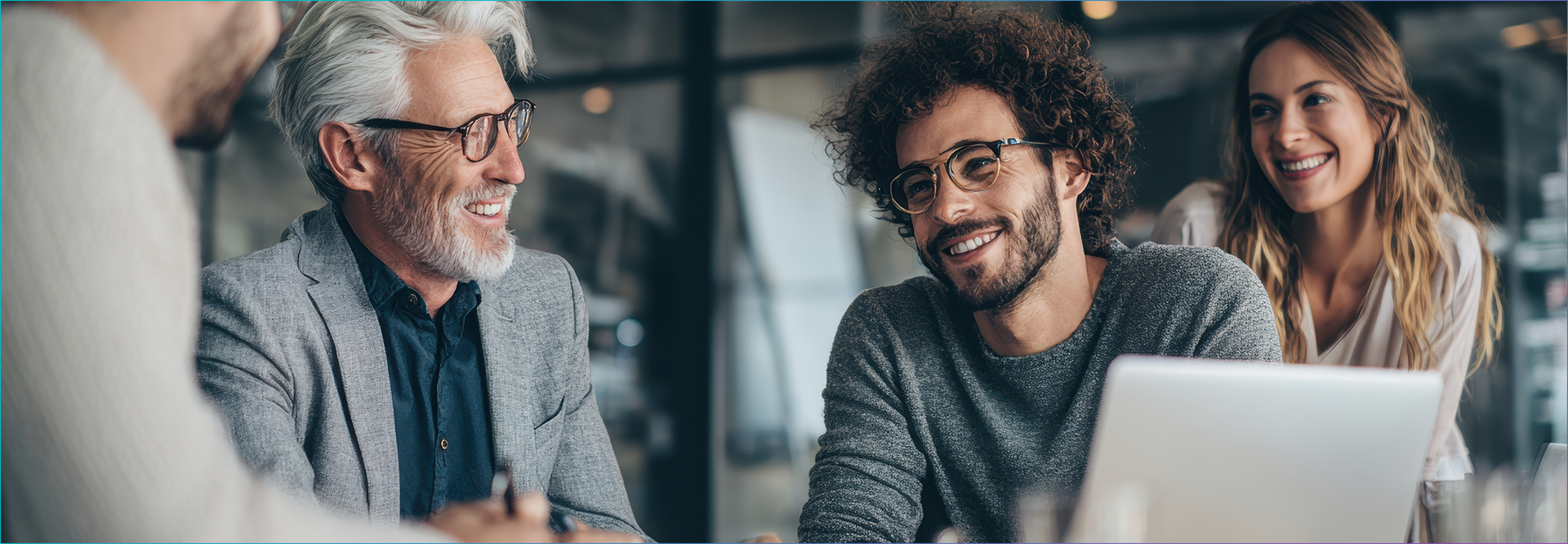 Quatro pessoas sentadas à mesa, sorrindo, olhando para um laptop.