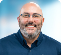 A bald man with glasses and a beard is smiling for the camera.