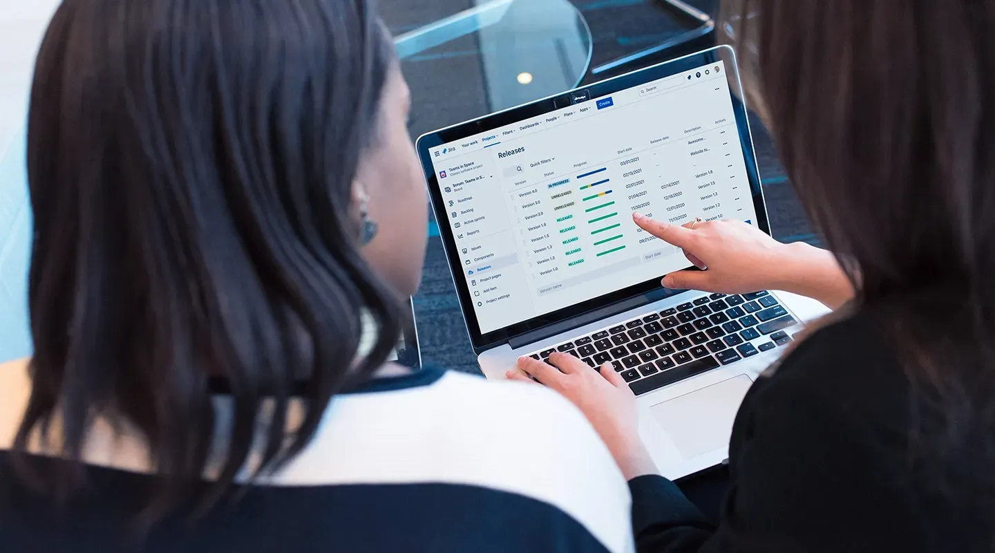 Two women are sitting at a table looking at a laptop computer.
