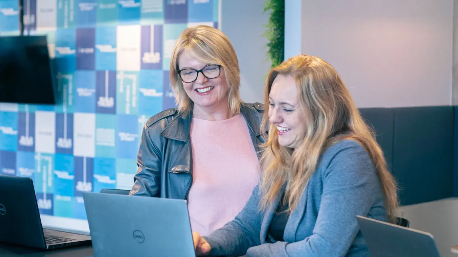 Two women are sitting at a table looking at a laptop computer.