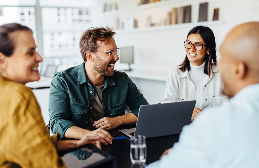 A group of people are sitting around a table with a laptop.