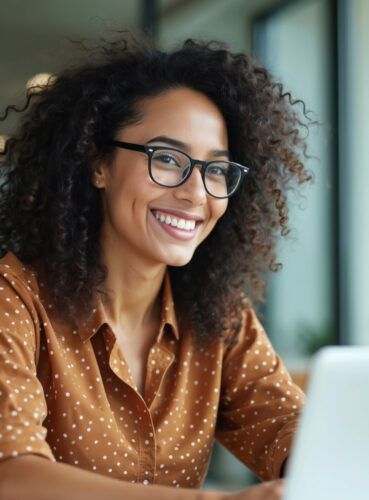 A woman wearing glasses is smiling while using a laptop computer.