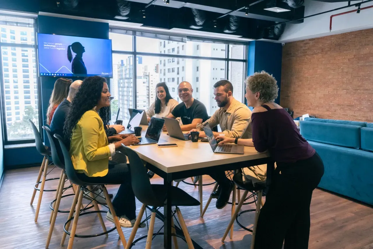 A group of people are sitting around a table with laptops.