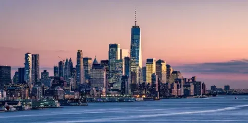 New York City skyline at dusk, with the One World Trade Center prominently featured.