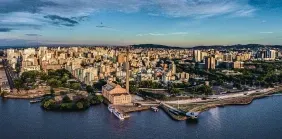 Cityscape with buildings along a waterfront under a blue sky, some clouds visible.