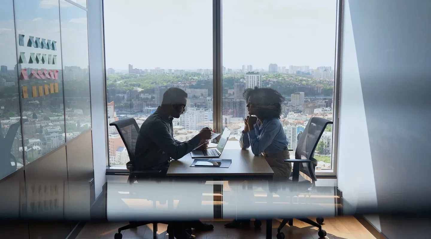 A man and a woman are sitting at a table in front of a window.