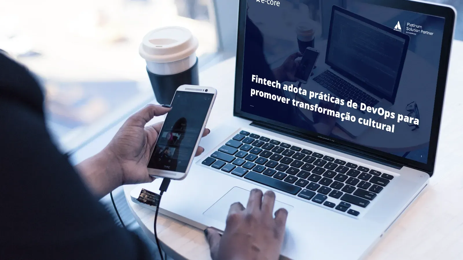 A person is using a laptop computer while holding a cell phone.
