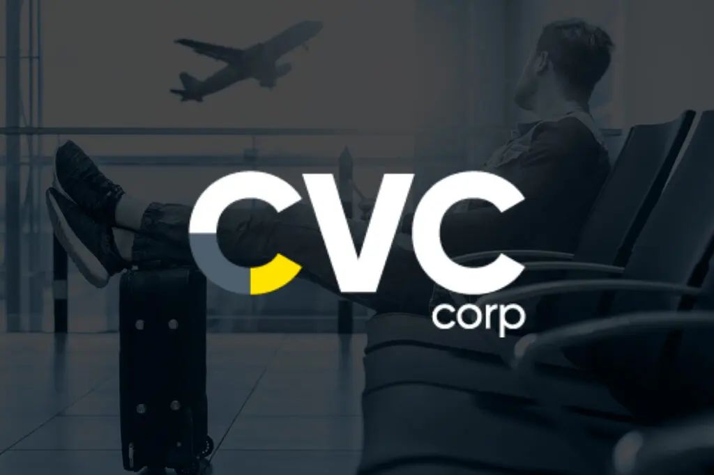 A man is sitting in an airport waiting area with a suitcase and a plane flying in the background.