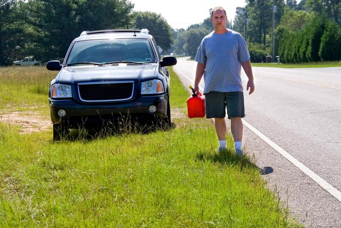 A man is standing on the side of the road holding a gas can.