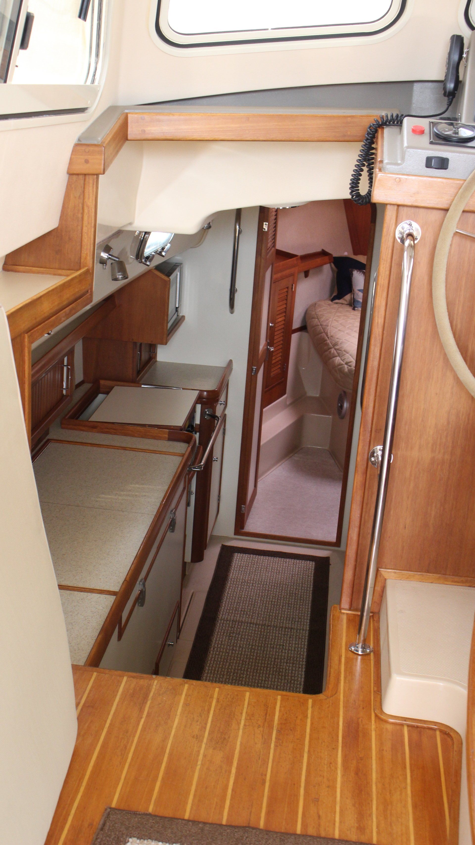 A kitchen on a boat with wooden floors and stairs leading to a bedroom.