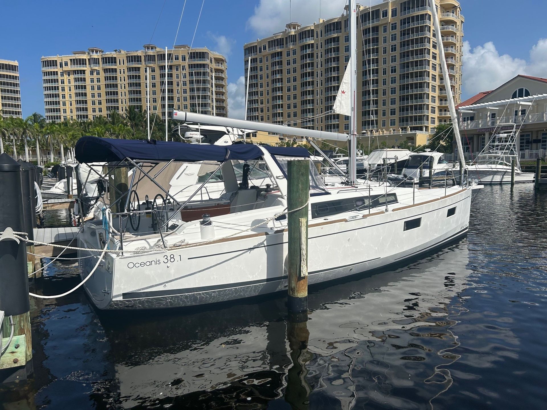 Sailboat docked in a waterway, white hull, blue canopy, buildings in the background on a sunny day.