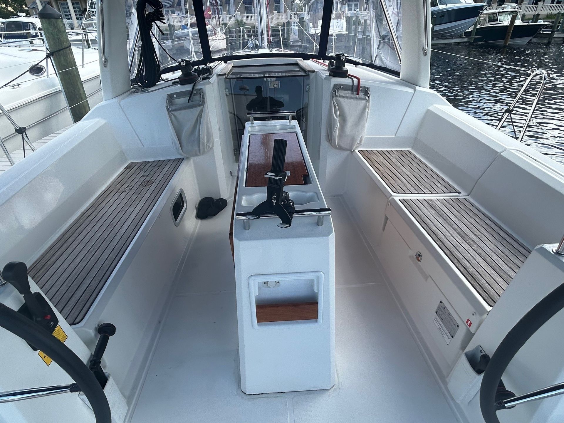 Cockpit of a sailboat with two steering wheels, white deck, and wooden benches.