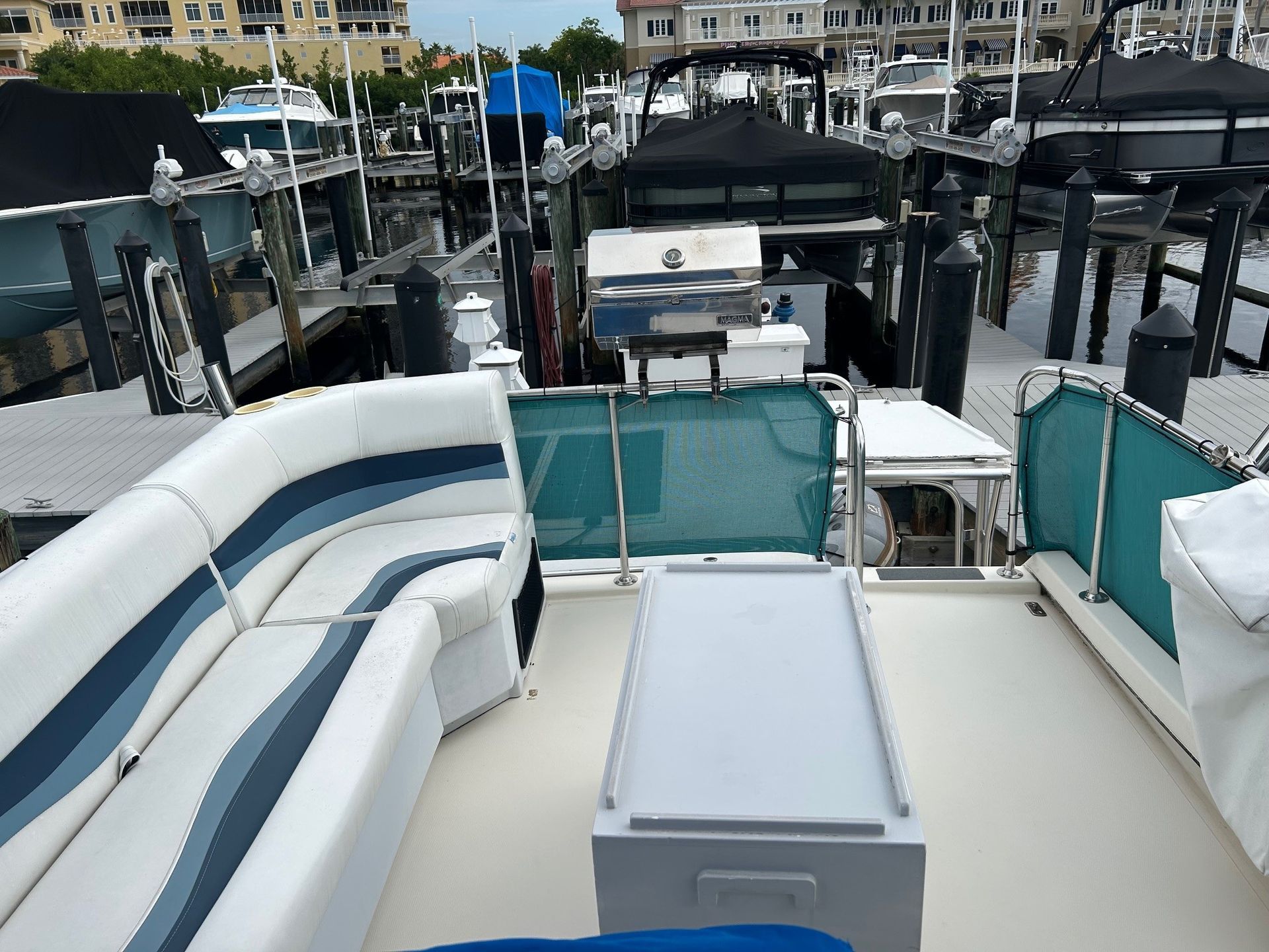 Boat deck with white and blue seating, grill, cooler, and dockside setting.